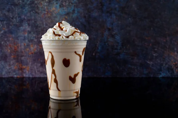 Vanilla milkshake with chocolate syrup in clear glass on dark background.