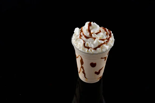 Vanilla milkshake with chocolate syrup in clear glass on dark background.