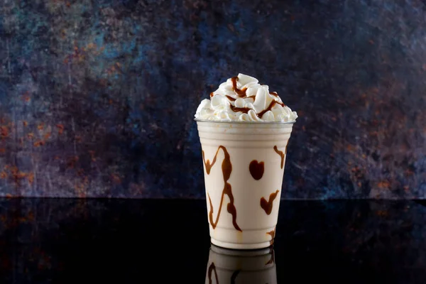 Vanilla milkshake with chocolate syrup in clear glass on dark background.