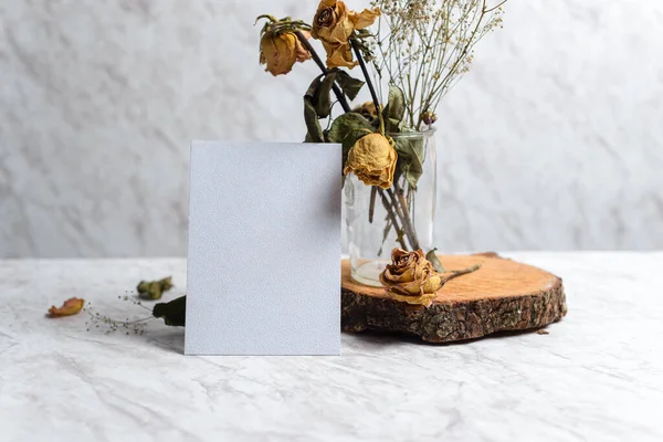 Blank card and wilted flowers on marble background. Concept of nostalgia, breakup, disappointment, separation.
