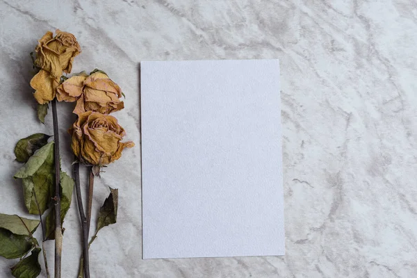 Blank card and wilted flowers on marble background. Concept of nostalgia, breakup, disappointment, separation.
