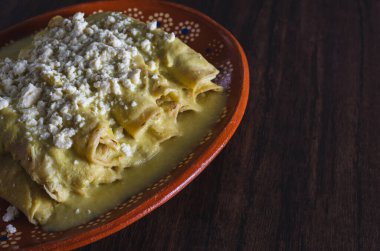 Green Enchiladas served in a clay dish on a wooden table. Typical Mexican food.