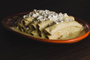 Green Enchiladas served in a clay dish on a wooden table. Typical Mexican food.