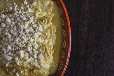 Green Enchiladas served in a clay dish on a wooden table. Typical Mexican food.