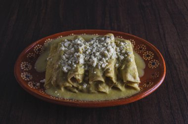 Green Enchiladas served in a clay dish on a wooden table. Typical Mexican food.