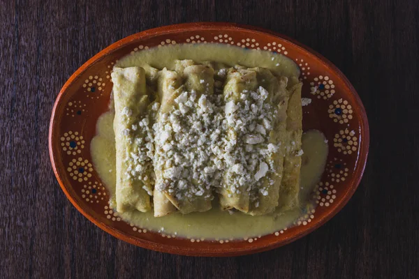 Yeşil Enchilada 'lar ahşap bir masada kil tabakta servis edilir. Tipik Meksika yemekleri..