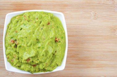 Guacamole served on white plate on wooden table. Insulated container with guacamole.
