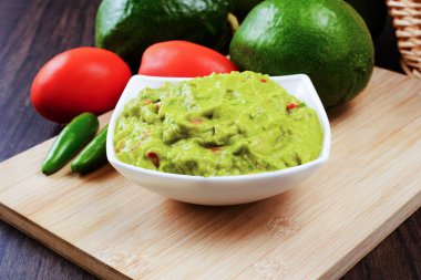 Guacamole served on a white plate on a wooden table. Guacamole ingredients.