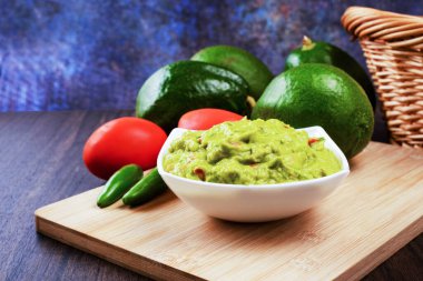 Guacamole served on a white plate on a wooden table. Guacamole ingredients.