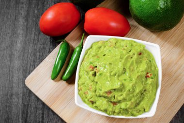 Guacamole served on a white plate on a wooden table. Guacamole ingredients.
