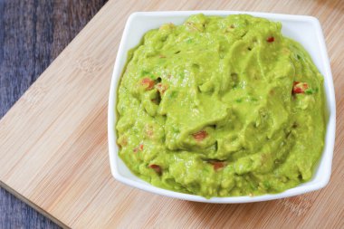 Guacamole served on white plate on wooden table. Insulated container with guacamole.