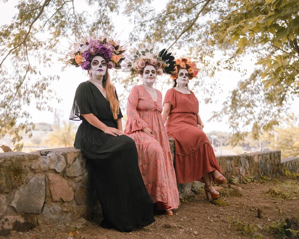 Group portrait of three women with the makeup of the catrinas.. Makeup for the celebration of Day of the Dead in Mexico. Outdoors portrait.