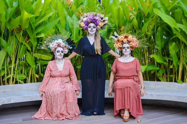 Group portrait of three women with the makeup of the catrinas.. Makeup for the celebration of Day of the Dead in Mexico. Outdoors portrait.