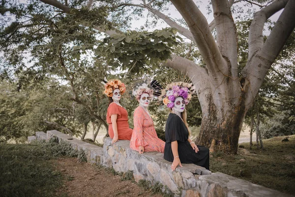 Group portrait of three women with the makeup of the catrinas.. Makeup for the celebration of Day of the Dead in Mexico. Outdoors portrait.