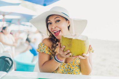 Hindistan cevizi suyu içen kadın. Plaj şapkalı kadın kamışla hindistan cevizi suyu içiyor..