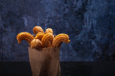 Siyah masada yansımalı şekerli churro. Kese kağıdında Churros. Mavi arkaplan.