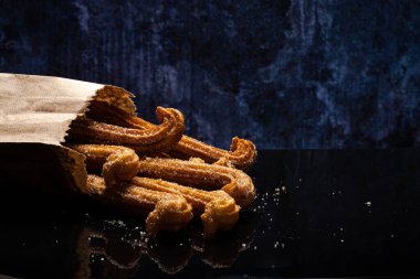 Siyah masada yansımalı şekerli churro. Kese kağıdında Churros. Mavi arkaplan.