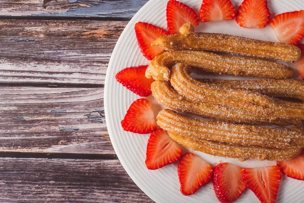 Ahşap bir masada beyaz bir tabakta çilekli Churros. Çilekle süslenmiş beyaz tepside şekerli Churros. Üst görünüm.