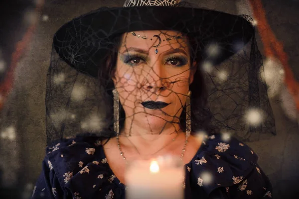Woman costumed as a witch holding lighted candle. Studio portrait of witch looking at camera on Halloween day.