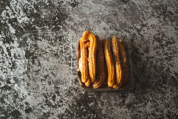 Churros in a plastic container on a cement table. Churros ready to eat.