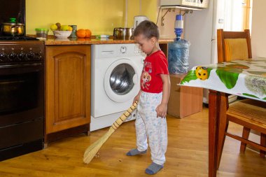 Küçük bir çocuk mutfak zeminini süpürgeyle süpürüyor.