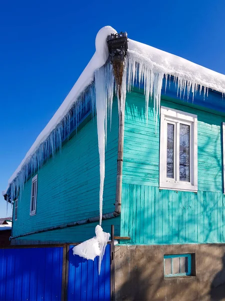 青い空を背景に村の家の屋根から吊るされた長いつらら — ストック写真