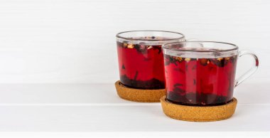 iki bardak çilek ve çiçek çayı mantarın üzerinde beyaz bir masanın üzerinde duruyor.