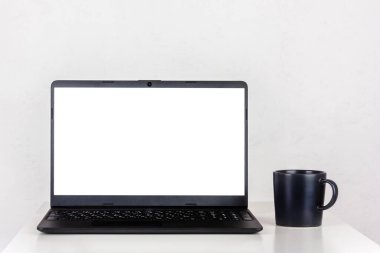 Bir dizüstü bilgisayar ekranında beyaz bir model ve masada siyah bir kupa çay fotokopi alanı olan beyaz bir duvara karşı.