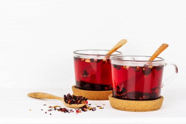 Mantar tezgahında ahşap kaşıklar olan iki bardak meyve ve çiçek çayı ve beyaz bir masada kuru çay kaşığı.