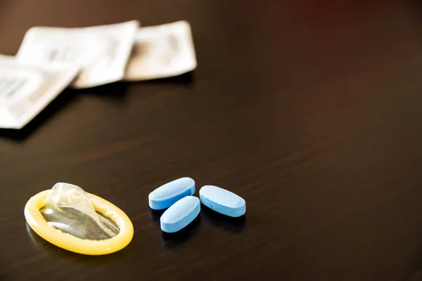 Blue pills to have a long-lasting erection, condom ready and in the background other condoms in pack on a dark background