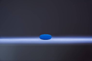 Single blue pill illuminated by a single sharp beam clipart