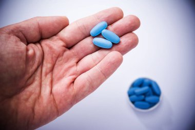 Erkek el, arka planda üç mavi hap ve mavi haplarla dolu bir kap gösteriyor.
