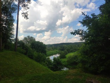Nehir ve ağaçlarla dolu tepe manzarası, yazın bulutlu güzel gökyüzü.