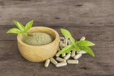 Andrographis Paniculata özü tahta kase, çay tabağı, yaprak ve bitkisel kapsüller, ahşap arka plan.