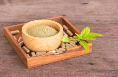 Andrographis Paniculata özü tahta kase, çay tabağı, yaprak ve bitkisel kapsüller, ahşap arka plan.