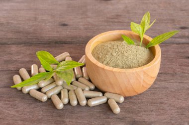 Extract powder of Andrographis Paniculata in wooden bowl, leaf, and herbal capsule on wooden background. clipart