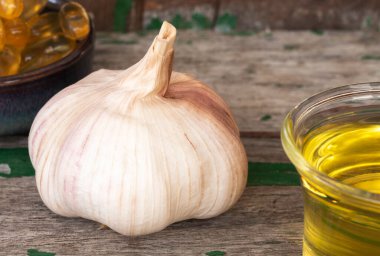 Sarımsak soğanı, yeşil kapsül yağı özü ve eski ahşap arka planda cam yağı, sarımsak birçok hastalığın riskini azaltmaya yardımcı olabilir. Sağlıklı yemek olarak sınıflandırılır.. 