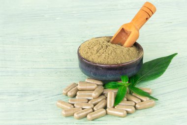 Andrographis Paniculata özüt tozu seramik kap içinde tıbbi bitki ve tahta kaşık, bitkisel kapsüller, ve taze yapraklar, eski yeşil ahşap arka planda.