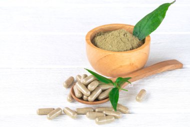 Andrographis paniklemiş bitkisel kapsüller, yaprak, tahta kaşık, kahverengi kasede panikleme özü tozu, ve beyaz ahşap arka plan.
