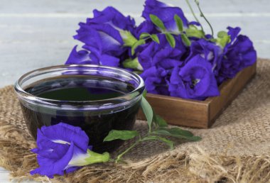 Taze mavi bezelye çiçeklerinden yapılmış mavi sağlıklı bir içecek ya da çuval bezi ve yeşil ahşap arka planda tahtadan bir tabakta kelebek bezelyesi..