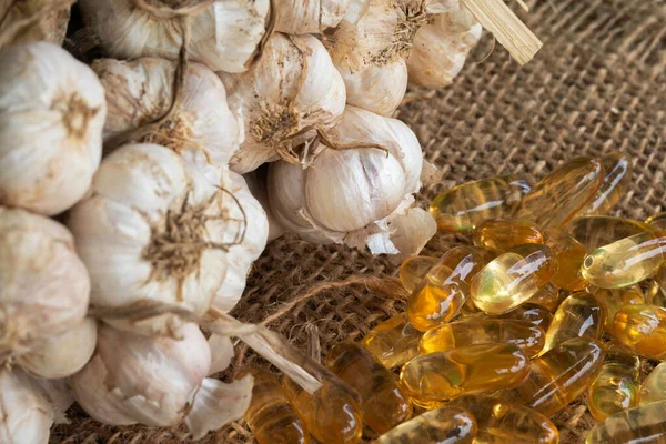 Transparent golden garlic oil capsules and fresh garlic bulb on brown sack background.