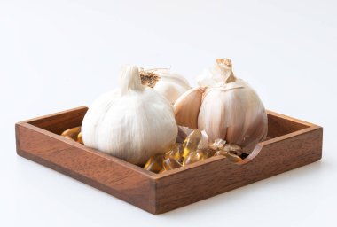 Sarımsak soğanları ve yağ kapsülleri, beyaz arka planda izole edilmiş, ahşap tabakta..