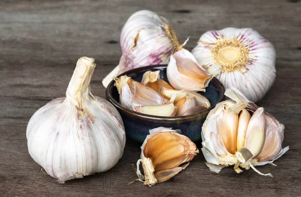 Garlic bulbs ( Allium sativum L.) and garlic cloves in ceramic bowl on old wooden background. Garlic prevents heart disease and reduces the risk of acute heart failure.