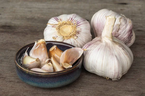 Garlic bulbs ( Allium sativum L.) and garlic cloves in ceramic bowl on old wooden background. Garlic prevents heart disease and reduces the risk of acute heart failure.