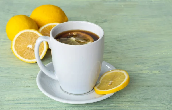 Black coffee, lemon slices, in white ceramic cup and yellow lemon on old wooden background.