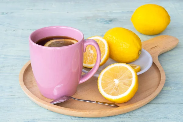 Black coffee, lemon slices in pink ceramic cup and yellow lemon on wooden saucer and on green wooden background.