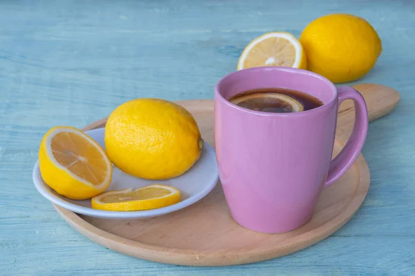 Black coffee, lemon slices in pink ceramic cup and yellow lemon on wooden saucer and on green wooden background.