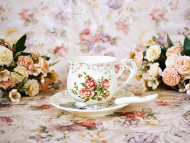 Antique cup of tea with saucer ,yellow orange rose flowers background ,porcelain vintage style ,old English coffee cup still life for wallpaper ,romance roses backgrounds 