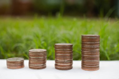 Bulanık yeşil çimen arka planına sahip ahşap üzerine bozuk para istiflemek. Plan nakit para kazanmak ve 2022 yeni yıl ve yatırım ve çevre koruma kavramı tasarruf finansman büyümesi.