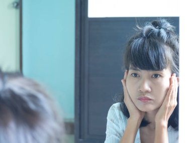 Kadın aynaya endişeli ve stresli bir şekilde bakıyor çünkü kırışıklıklar ve yüzünde koyu lekeler var. Otantik siyah saç ve ten rengi Asya Tayland. Yaşam tarzı sağlık ve güzellik konsepti.